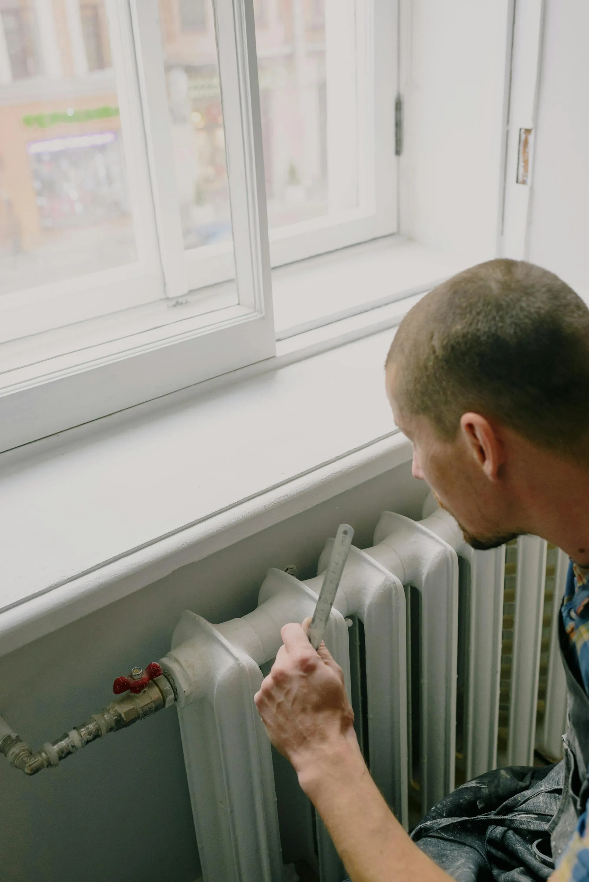 Heating engineer working on a radiator beside a sash window in a Bradford terrace
